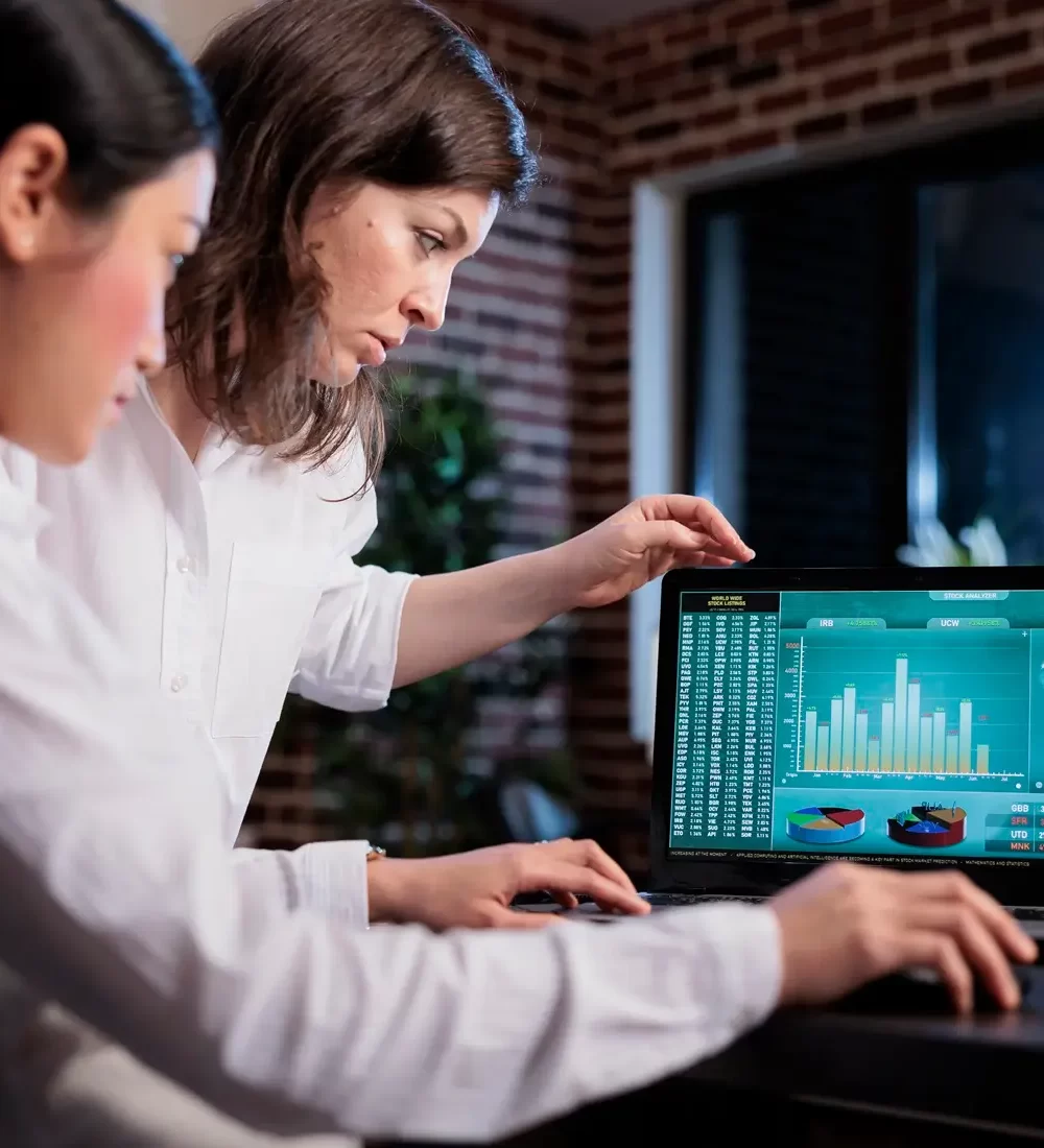 Funcionários de agência de marketing discutindo sobre consultas enquanto analisam dados financeiros no laptop